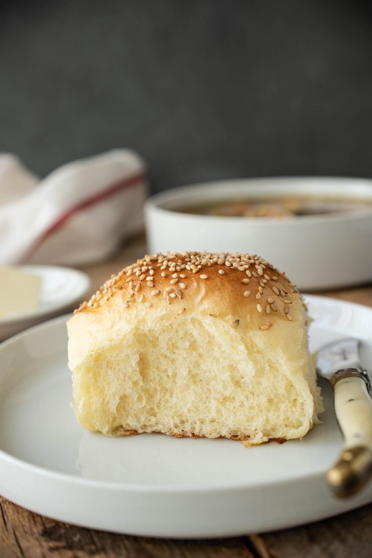 A sesame bread roll on a white plate with a butter knife