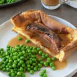 A piece of toad in the. hole on a plate with fresh peas