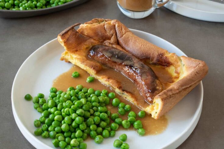 A piece of toad in the. hole on a plate with fresh peas