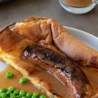 Toad in the Hole with 1 sausage on a plate with onion gravy and green peas