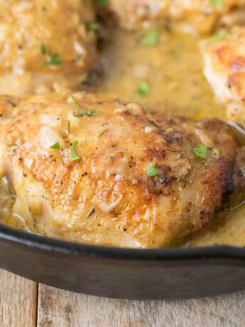 A closeup of a browned chicken thigh in a cast iron pan bathed in Dijon sauce
