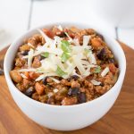 A white bowl full of turkey and bean chili topped with cheddar cheese and cilantro