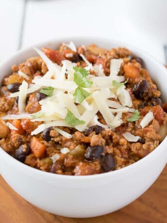 A white bowl full of turkey and bean chili topped with cheddar cheese and cilantro