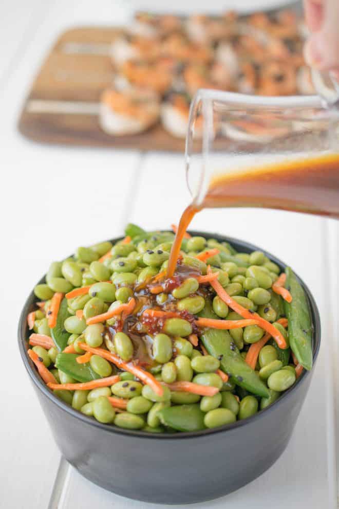 Pouring sesame ginger dressing over edamame and snap peas