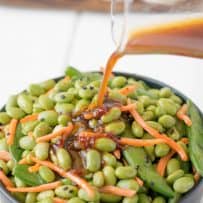 Sesame ginger dressing being poured over edamame and snap peas