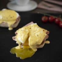 English muffin topped with sliced mortadella, poached egg and hollandaise which is an eggs benedict