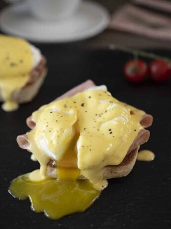 English muffin topped with sliced mortadella, poached egg and hollandaise which is an eggs benedict