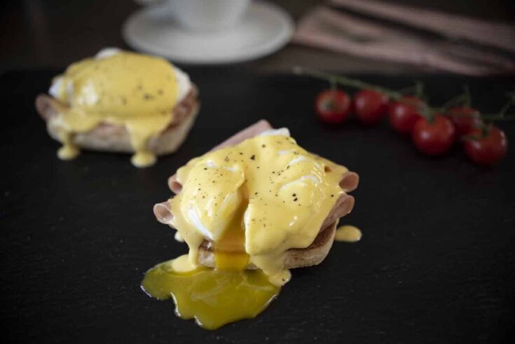 English muffin topped with sliced mortadella, poached egg and hollandaise which is an eggs benedict