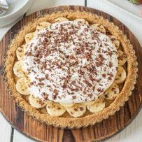 Banoffee pie on a round wood board with fresh strawberries