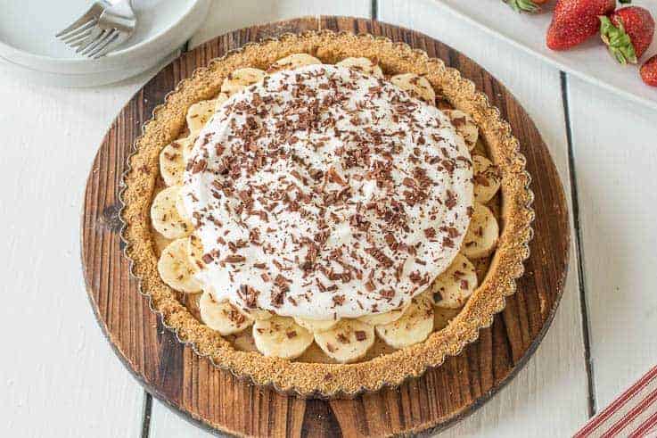 Banoffee pie on a round wood board with fresh strawberries