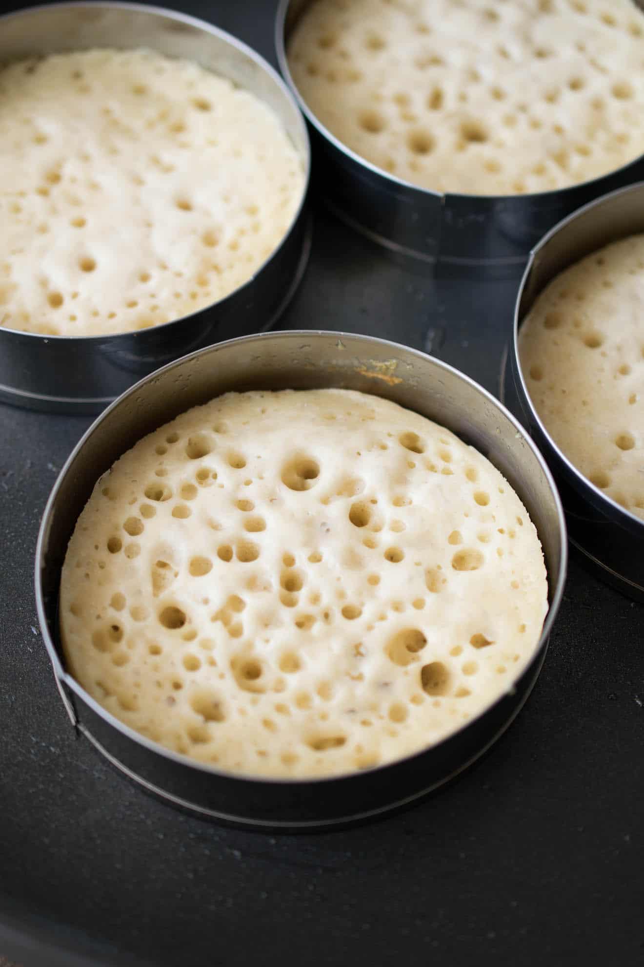 Crumpet dough in ring molds cooking in a pan showing the holes