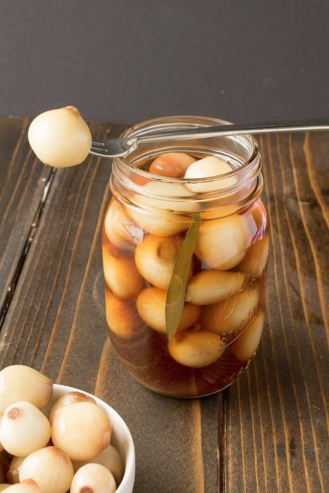A jar of English pickled onions with one onion on a fork