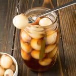 A pickled onion on a fork resting on a jar of English pickled onions