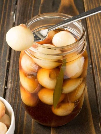 A pickled onion on a fork resting on a jar of English pickled onions