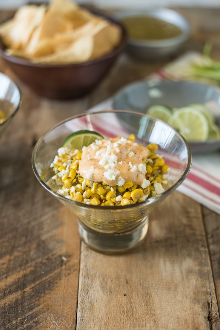 A glass bowl filled with Esquites Mexican Corn Salad with fresh limes