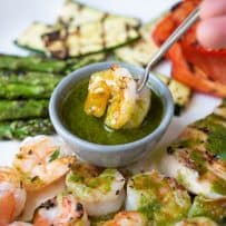 Dipping a grilled shrimp into a bowl of herb sauce