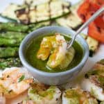 Green herb sauce in a small bowl with a shrimp on a fork being dipped into it surrounded by vegetables