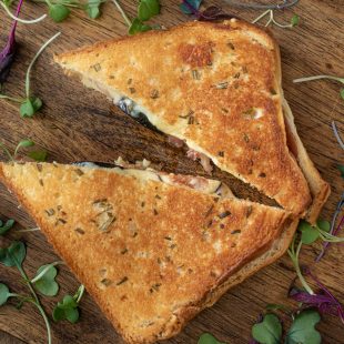Fig and prosciutto grilled cheese cut in half garnished with micro greens