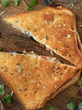 Fig and prosciutto grilled cheese cut in half garnished with micro greens