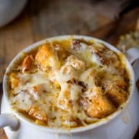 Lots of melted gruyere cheese over croutons that top a French onion soup in a white soup bowl