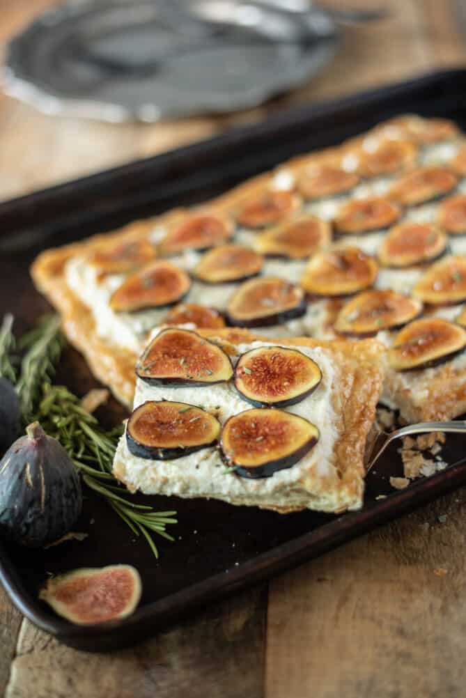 A slice of fig and ricotta tart on a spatula with fresh fig and rosemary garnish
