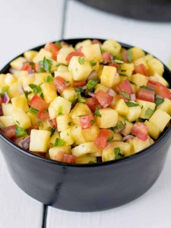 A black bowl filled with fresh pineapple salsa