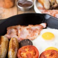 Halves of tomato, cooked mushrooms, sausage, bacon and eggs in a frying pan