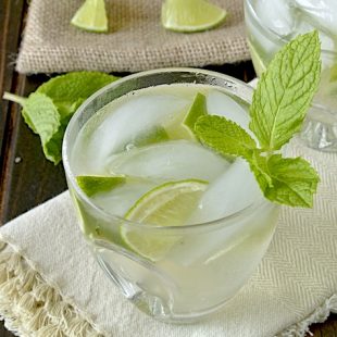 A glass of Ginger Gin Fizz in a short glass garnished with lime and mint