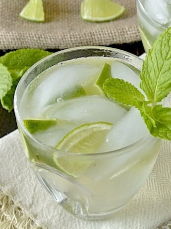 A glass of Ginger Gin Fizz in a short glass garnished with lime and mint