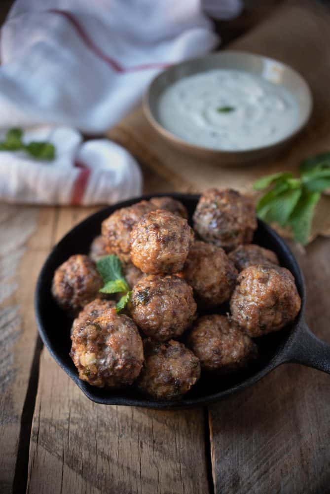 A cast iron skillet filled with Greek meatballs garnished with fresh mint leaves