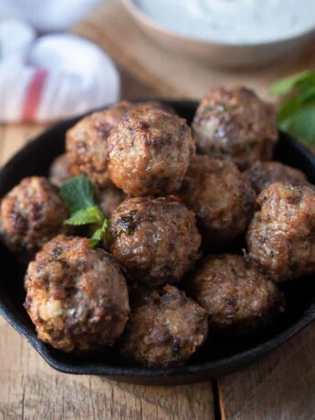 A black skillet full of browned meatballs