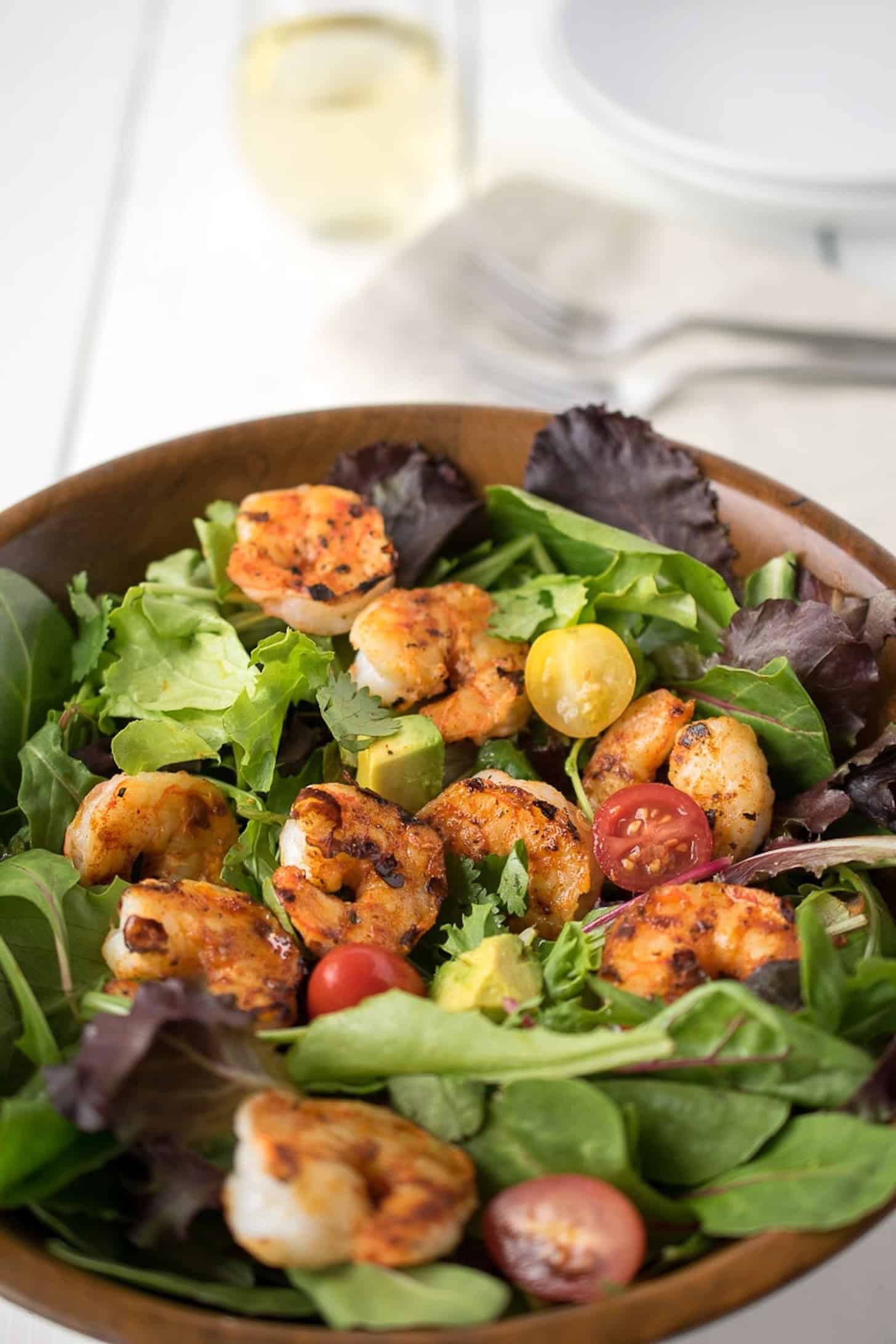 A wooden bowl filled with salad greens, cherry tomatoes and blackened shrimp