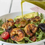 Pouring green cilantro dressing over shrimp and salad