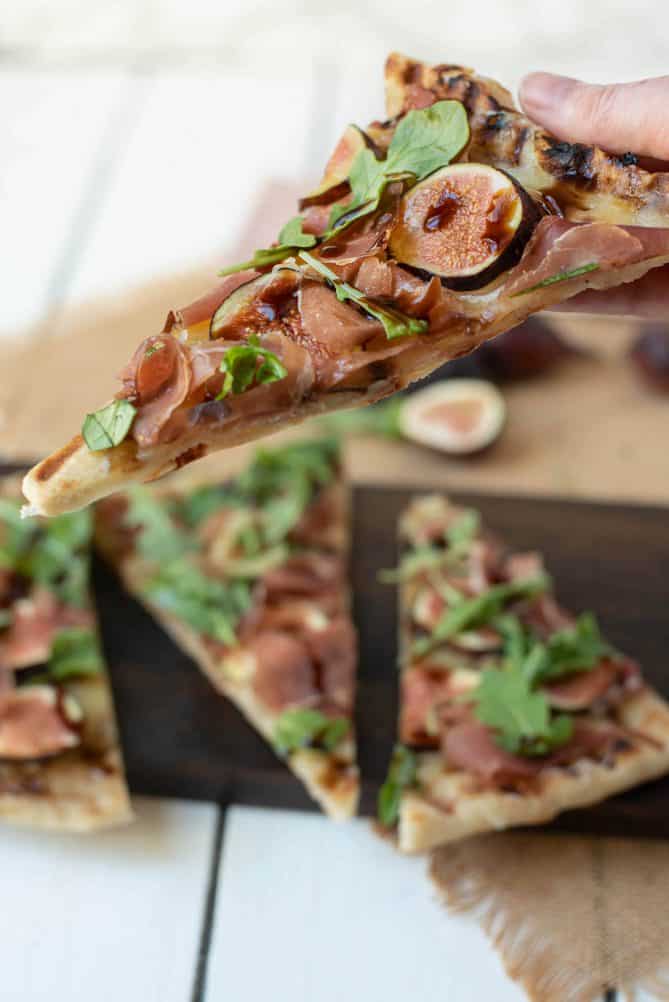 Holding a slice of fig, flatbread with arugula, prosciutto and balsamic glaze