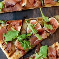 Green arugula on top of fresh sliced figs, sliced prosciutto on grilled flatbread sliced into triangles