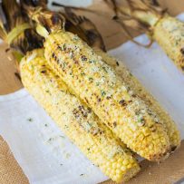 Grilled Parmesan, garlic and basil corn on the cob is a delicious use of sweet, seasonal corn. Sweet corn is grilled then topped with fresh Parmesan, a butter made with roasted garlic and fresh basil for the best barbecue side dish.