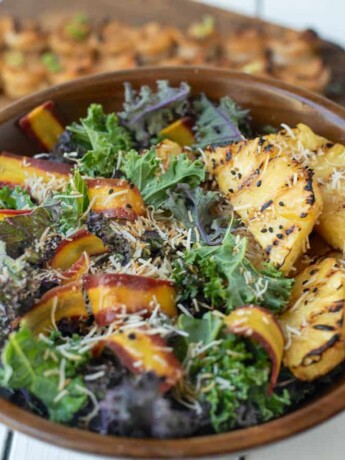 Slices of grilled pineapple on a bed of kale with shaved carrot and toasted coconut