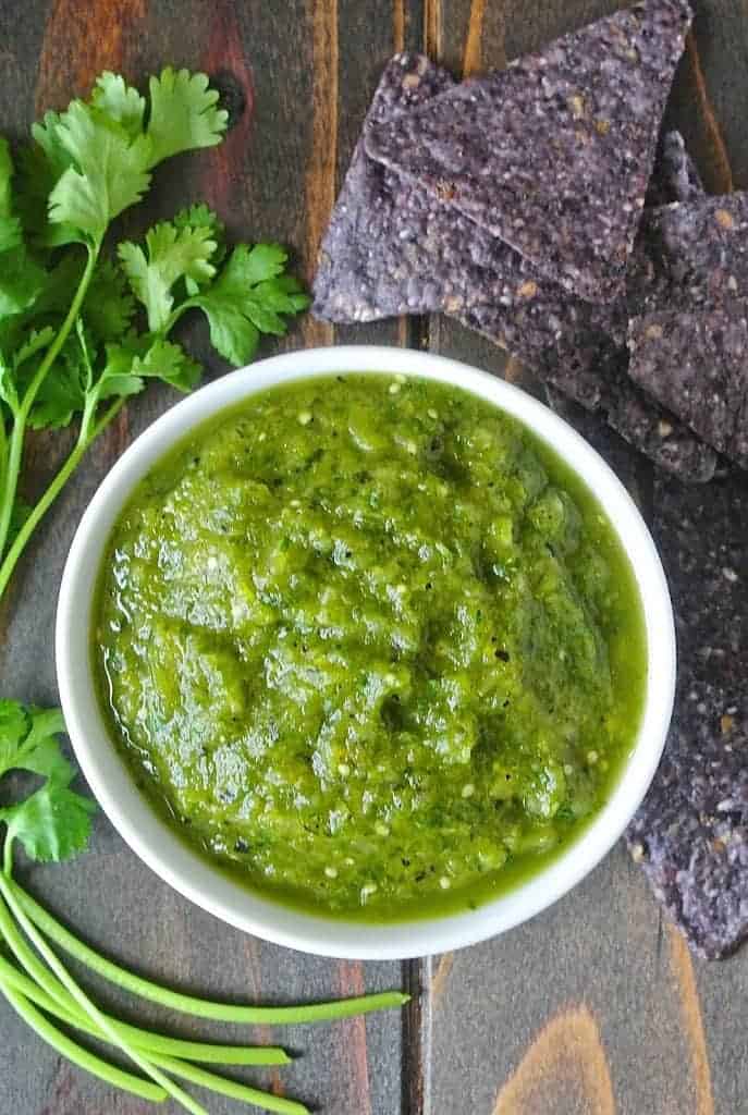 Vibrant green grilled salsa verde in a white bowl with blue corn chips and cilantro