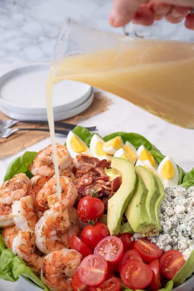 Pouring salad dressing over a grilled shrimp cobb salad