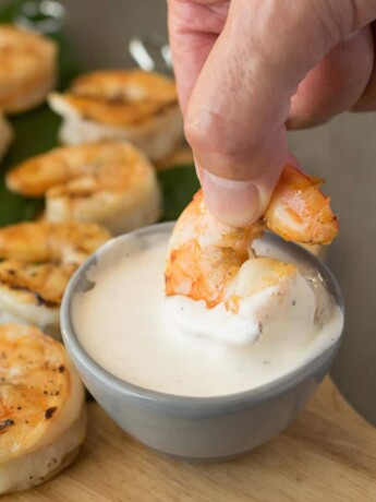 dipping a grilled shrimp into a white sauce