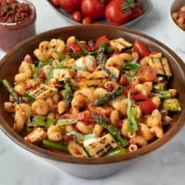 A large wood bowl filled with grilled vegetable sun-dried tomato pesto pasta with asparagus, red peppers, zucchini, spring onions and tomatoes