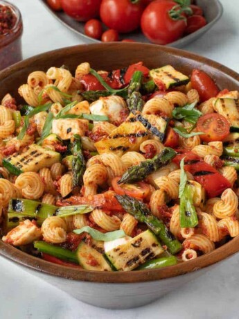 A large wood bowl filled with grilled vegetable sun-dried tomato pesto pasta with asparagus, red peppers, zucchini, spring onions and tomatoes