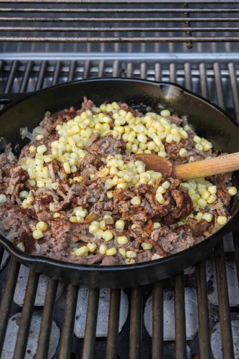 Ground beef and corn cooking in a cast iron skillet on a grill