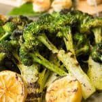 A tray of grilled broccoli with lemon and shrimp