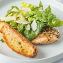 A large crouton with Caesar salad and a chicken breast on a white plate