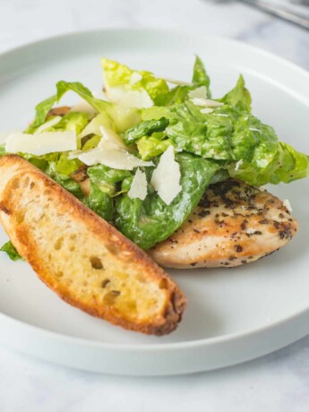 A large crouton with Caesar salad and a chicken breast on a white plate