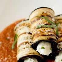 A closeup of grilled eggplant rollatini topped with fresh basil and Parmesan cheese