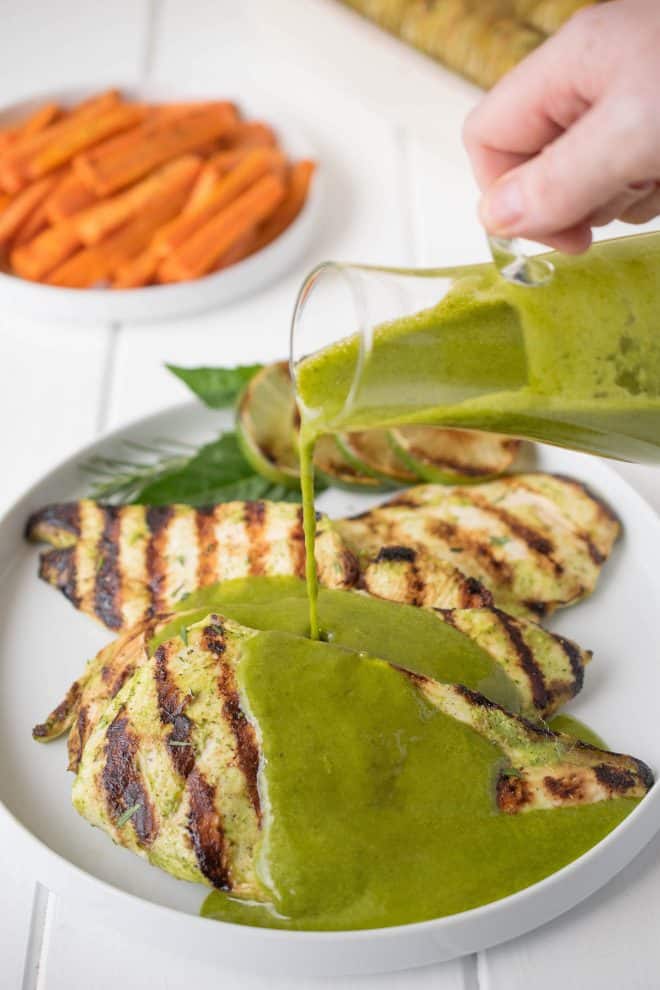 Pouring herb sauce over grilled chicken breasts