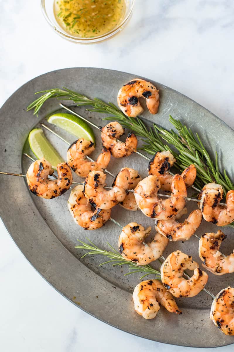 Skewers of grilled key lime shrimp on a pewter plate garnished with fresh rosemary and lime wedges