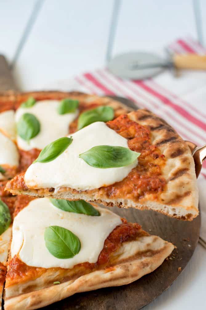 Serving a slice of grilled Margherita pizza topped with sauce, fresh mozzarella and fresh basil